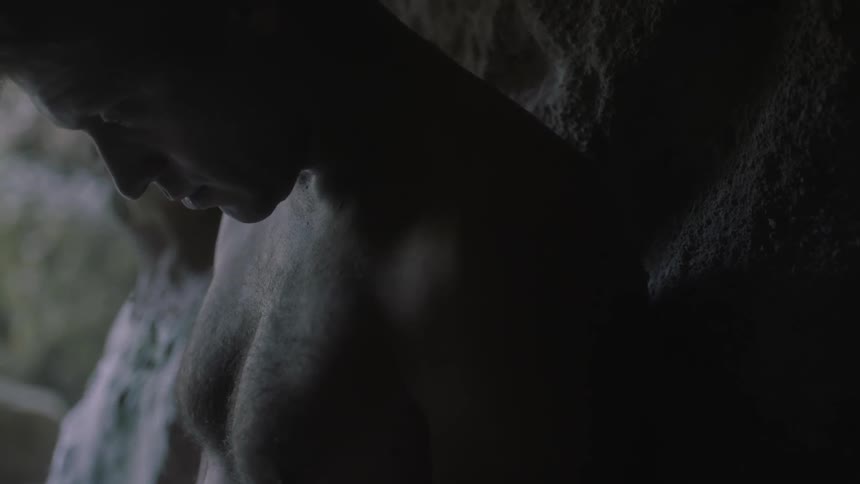 A man is leaning against the entrance of a cave