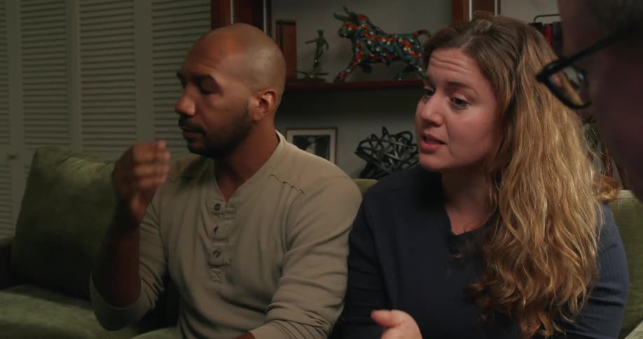 Woman with brown hair and bald man with beard and gray sweater argue with each other sitting on couch in living room next to man wearing glasses