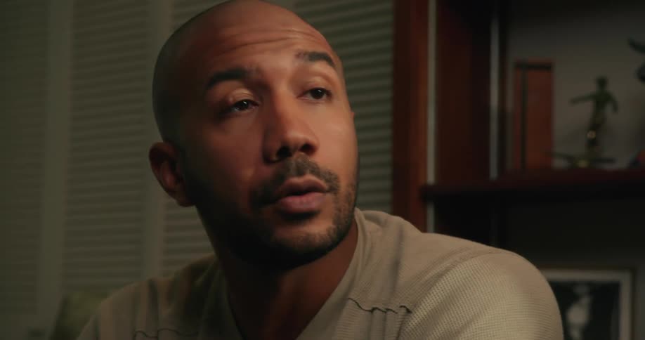 Bald man with beard and gray sweatshirt talks to person discussing plans in the living room