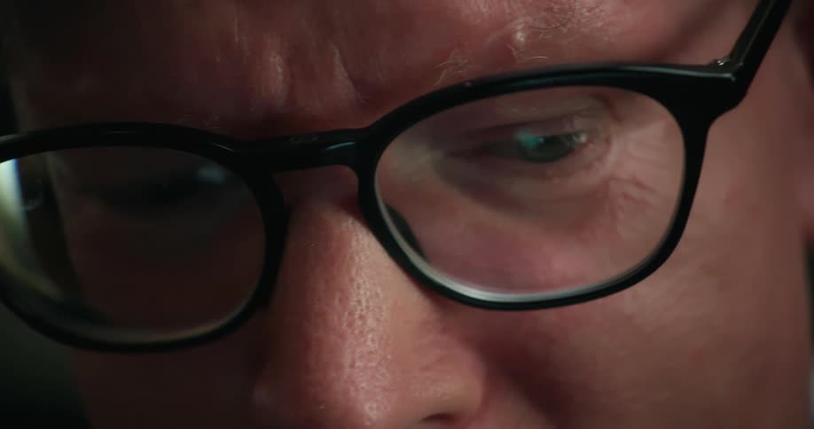 A man wearing glasses looks downward while reviewing information