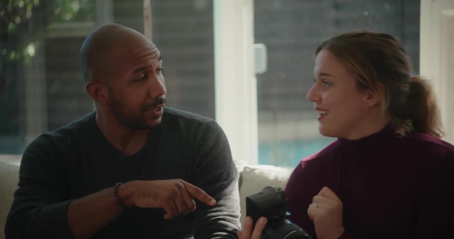 A couple talking on a couch while the female holds a camera
