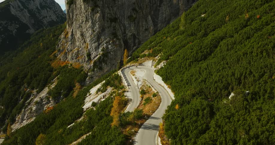 Two cyclists ride down a road that winds through a mountain range