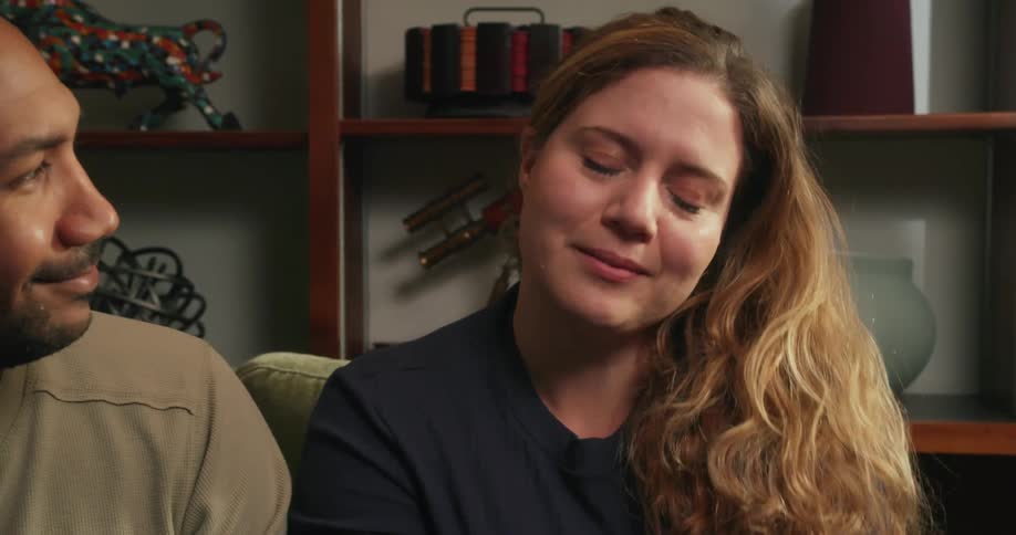 A man and woman sit together on a couch an d hold hands while talking to another person