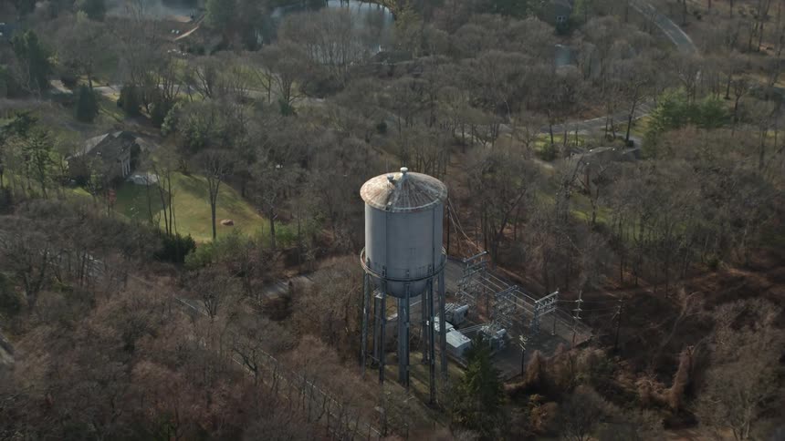 Fly over leafless trees and approach a water tower in Brookville Long Island New York during winter