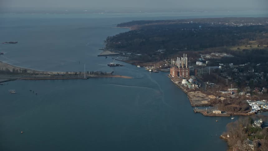 Aerial footage of Hempstead Harbor in Glenwood Landing Long Island with a power plant and smoking stacks visible on the shoreline during winter