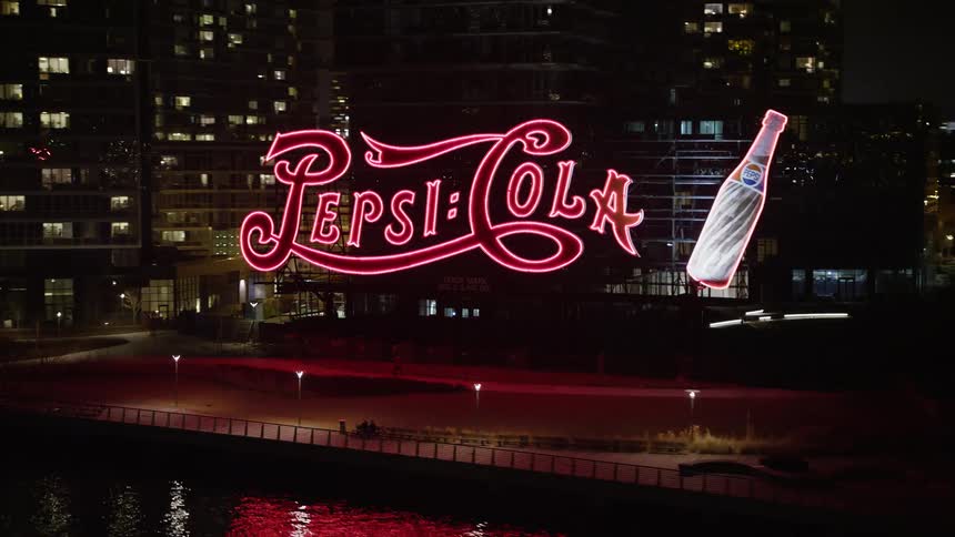 A low flying 4K aerial clip at night of the famous Pepsi sign and riverfront apartment buildings in winter Queens New York City