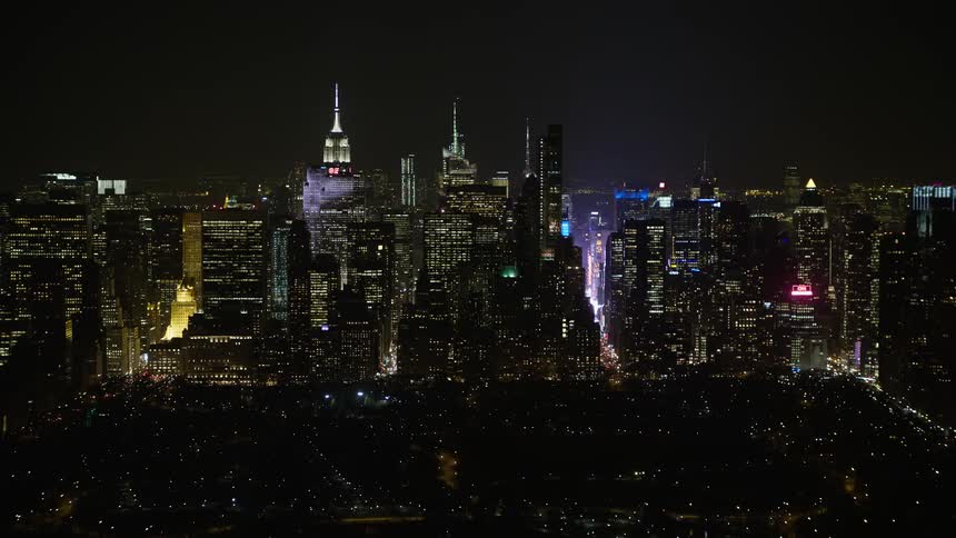 A nighttime aerial view of towering skyscrapers and bustling streets in New York City viewed from Central Park during the winter season