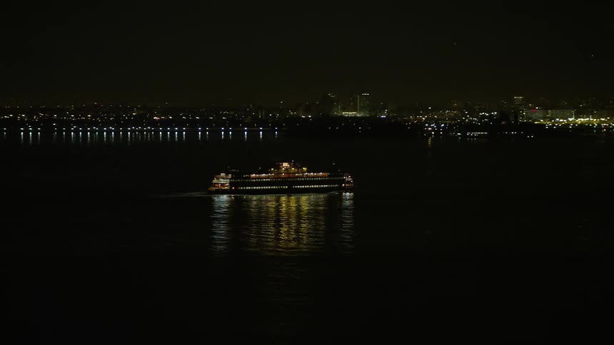 A Staten Island Ferry sails New York Harbor at night during winter passing by a well-lit pier