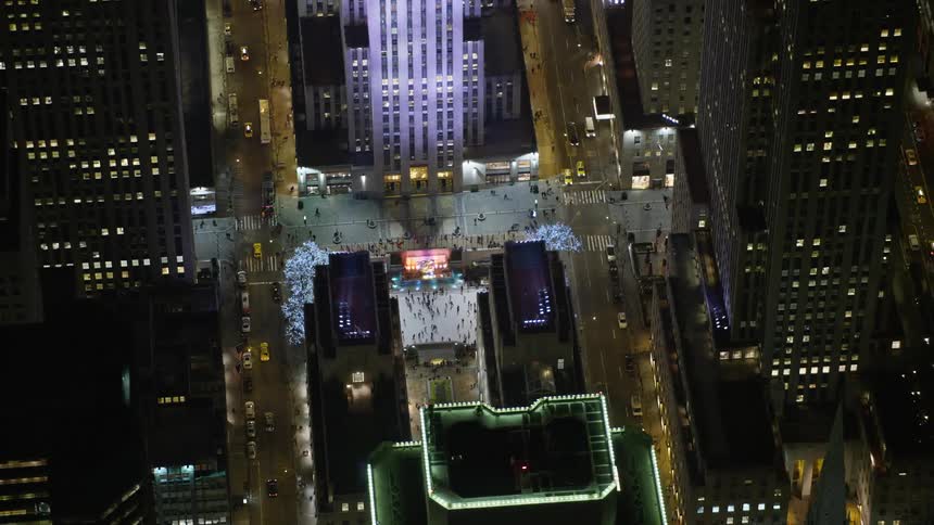 Aerial footage of Rockefeller Center skyscraper orbiting to reveal the ice skating rink at night in Midtown Manhattan New York City during winter