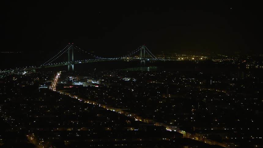 An aerial footage at night of Verrazano-Narrows Bridge and illuminated buildings in New York City seen from Brooklyn neighborhoods during winter