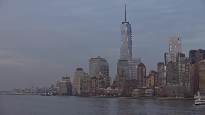 Aerial view of Lower Manhattan skyline with the World Trade Center and One World Trade Center as a ship moves through the water during sunset