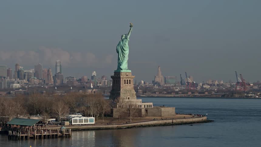 An orbiting aerial view of the Statue of Liberty on Liberty Island in New York Harbor revealing the Lower Manhattan skyline in the background during winter without snow