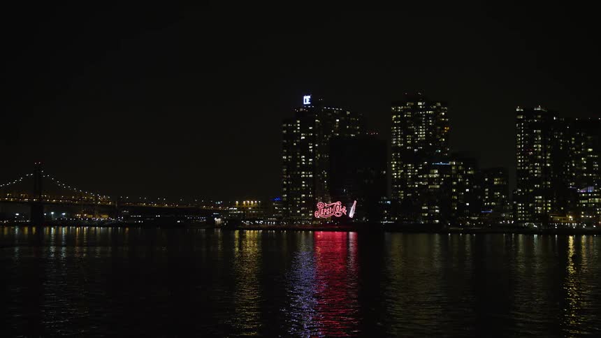 Approaching the iconic Pepsi sign and waterfront apartment buildings of Queens New York City at night during the winter season