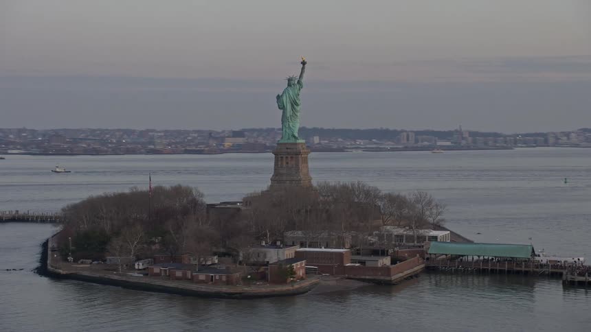 Aerial footage of the iconic Statue of Liberty and Island during a cloudy winter twilight in New York