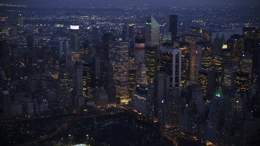 Aerial view at twilight of large group of skyscrapers in Midtown Manhattan New York City during winter highlighted by glowing lights from tall buildings and superstructures