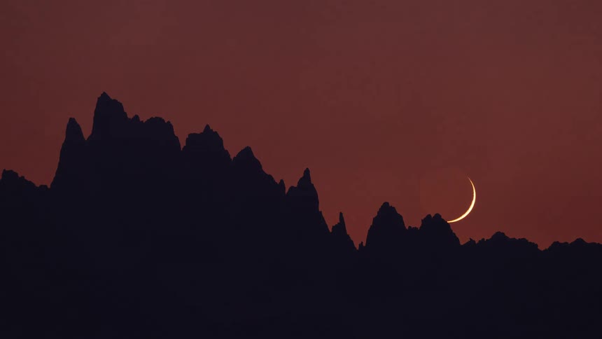 The moon sets behind the mountain