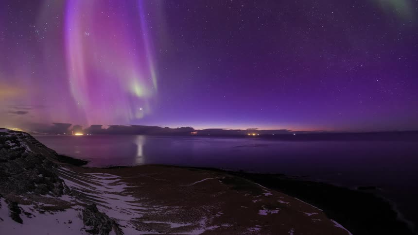 Colorful polar lights floating and shimmering over a river near a town at evening