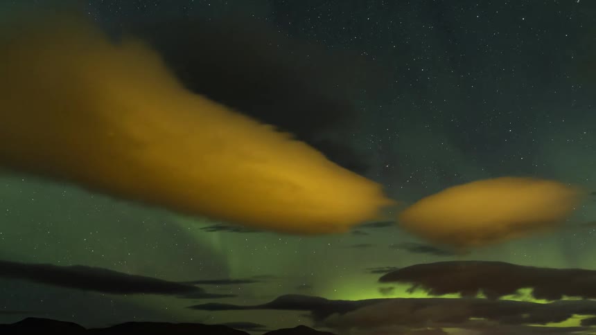 Clouds float among the green lights of the aurora borealis as they move across the night sky
