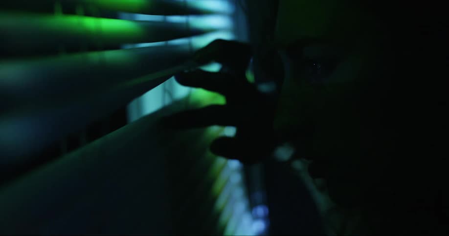 A young woman timidly peeks out the window at the bright and colorful lights outside