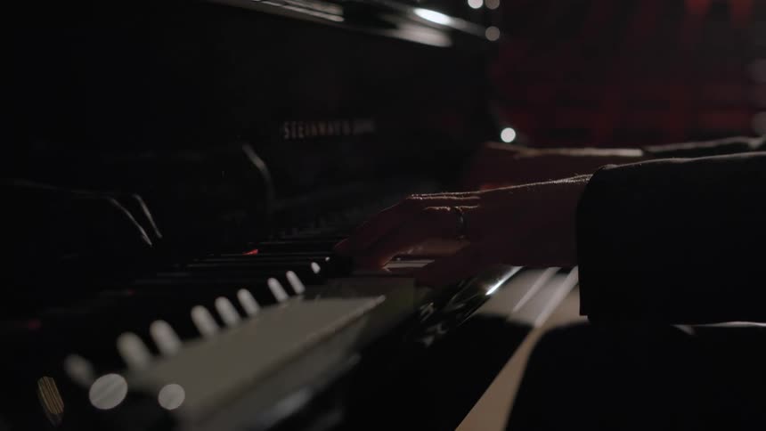 A man is sitting at a piano and playing music with both hands on the keys