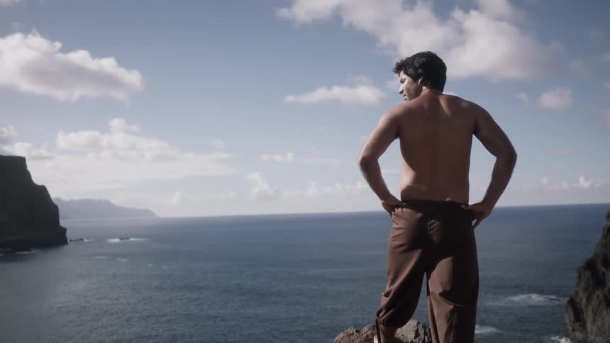 A man stands on a rock looking over the water