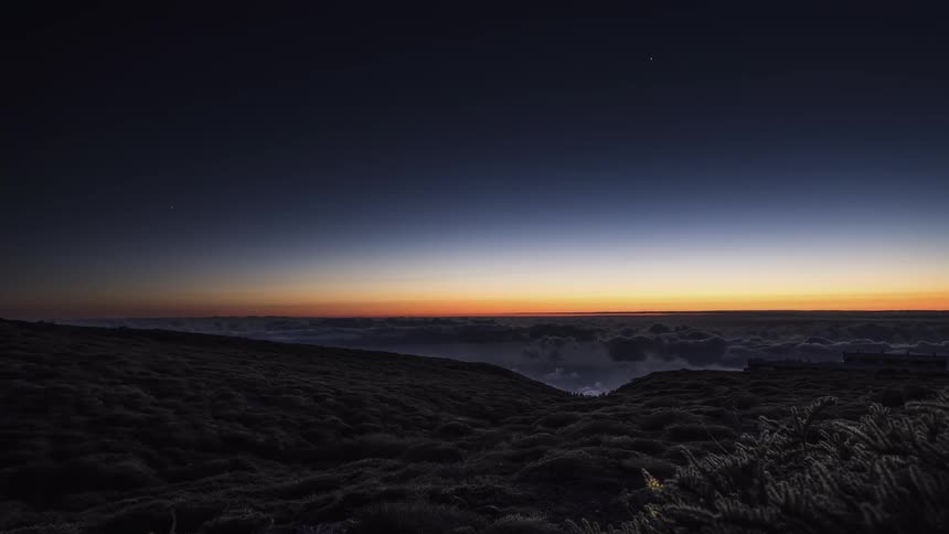 Clouds move along a mountaintop as the sun glows on the horizon