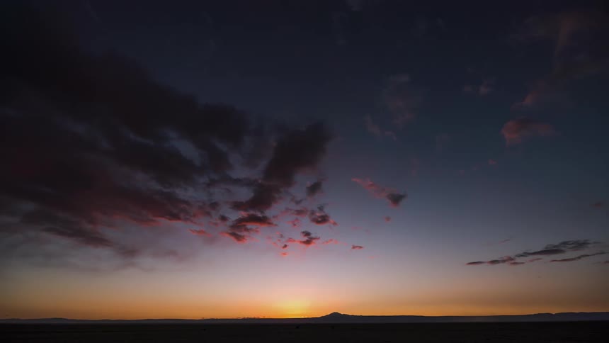 Clouds move in the sky and reflect the colors from the sunset on the horizon