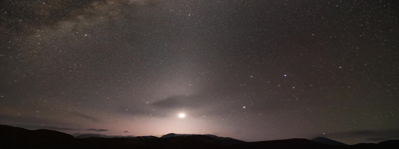 Light clouds move above the ground as the stars in the milky way light up the night sky until the sun rises and they sky is blue