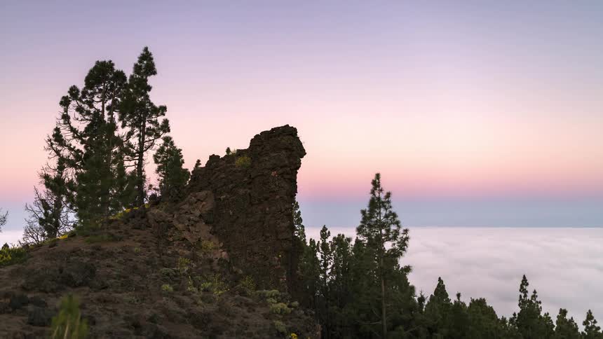 The sun rising over a rock formation and trees in the mountains
