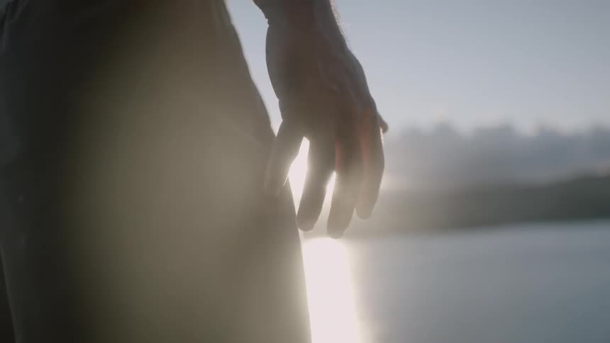 A person lifts their hand up by a lake at sunset
