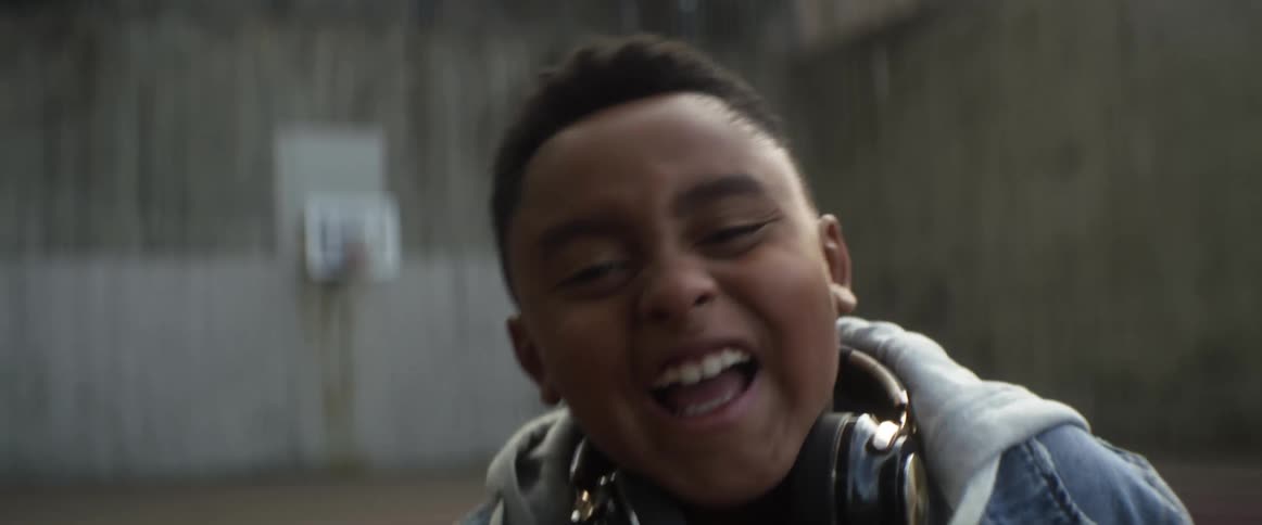 A boy laughs while looking into the camera on an outdoor basketball court
