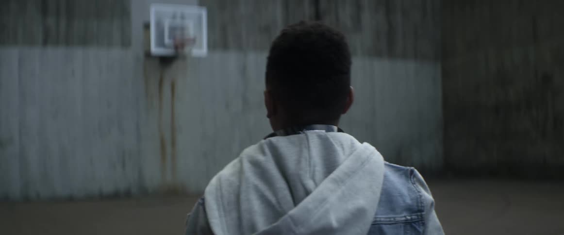 Boy with denim jacket walks in basketball court