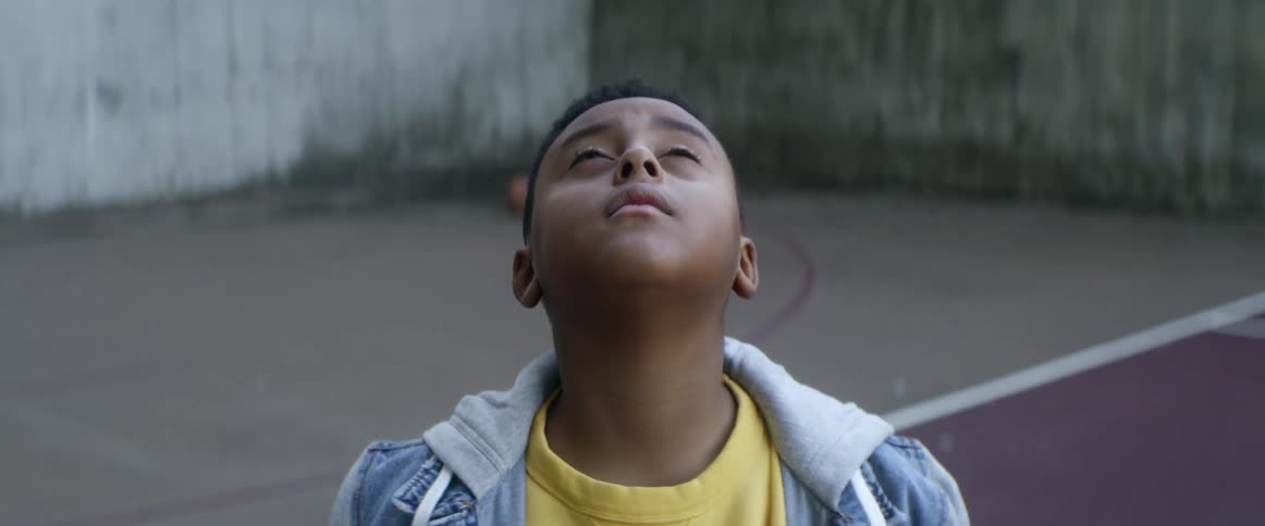 Closeup of boy wearing yellow t shirt and denim jacket looks up in the sky in the basketball court
