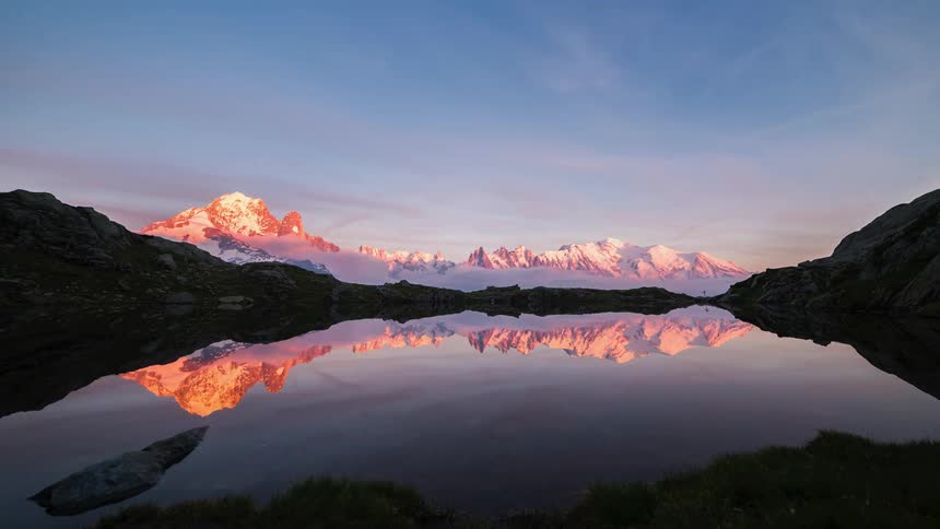 Clouds reflect off a lake as they move over a mountain range