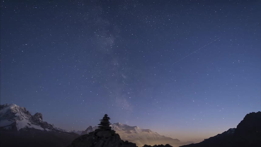 Clouds move around mountains as the sun sets and the milky way appears in the sky