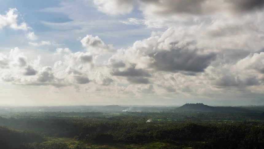 Cumulus clouds move over land with a mountain in the distance