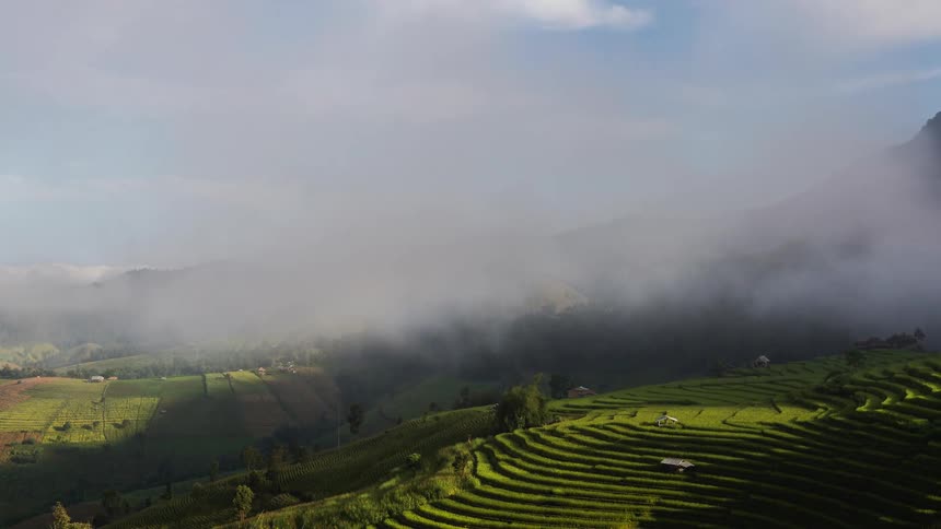 Aerial view of clouds floating over farmlands on hill slope