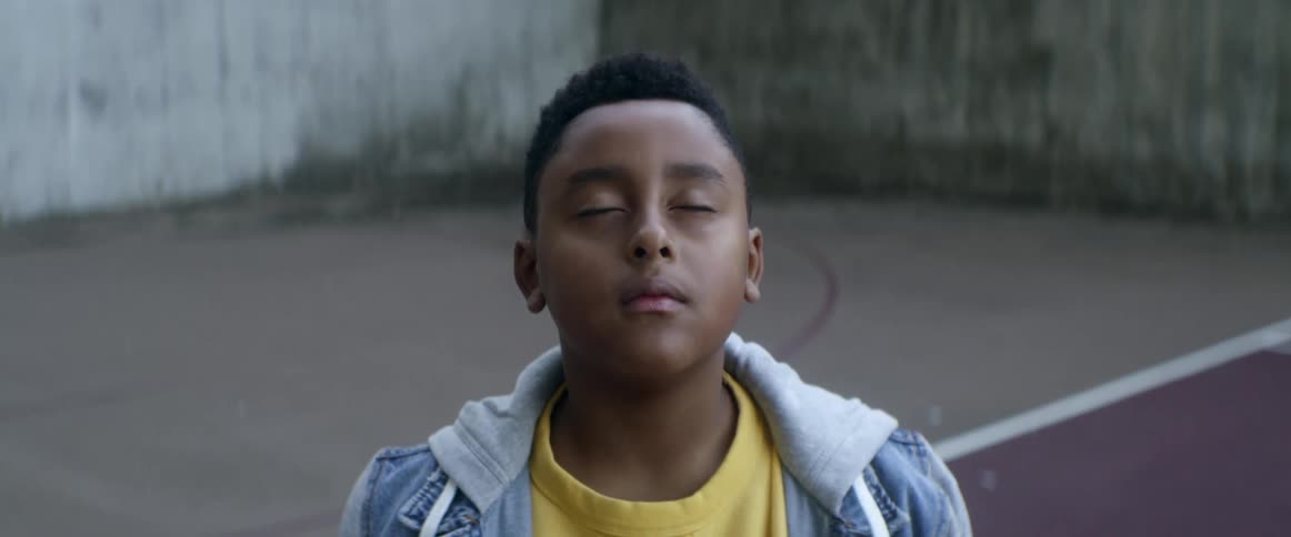 A basketball rolls behind a boy while he stands on a basketball court