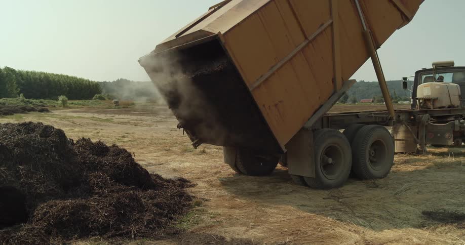 A truck dumps a trailer full of dirt on the ground