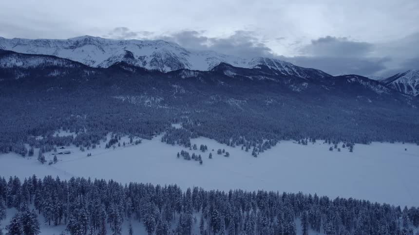 A snow capped mountain ridge with tree covered slopes and a road in the snow covered valley