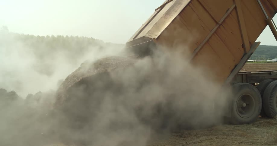 Truck dumping steaming piles of manure on a field at daytime