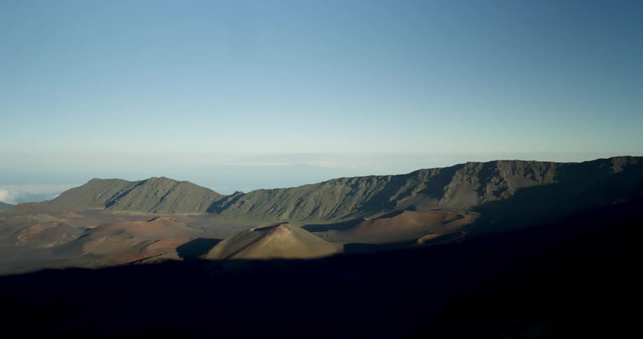 Morning shadows cover the slopes of a mountain range at sunrise