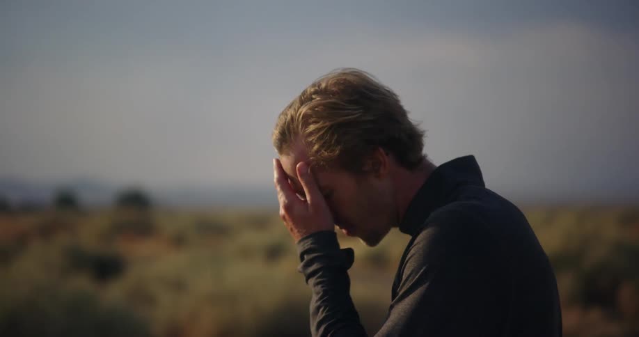 A man rubs his face while standing outside