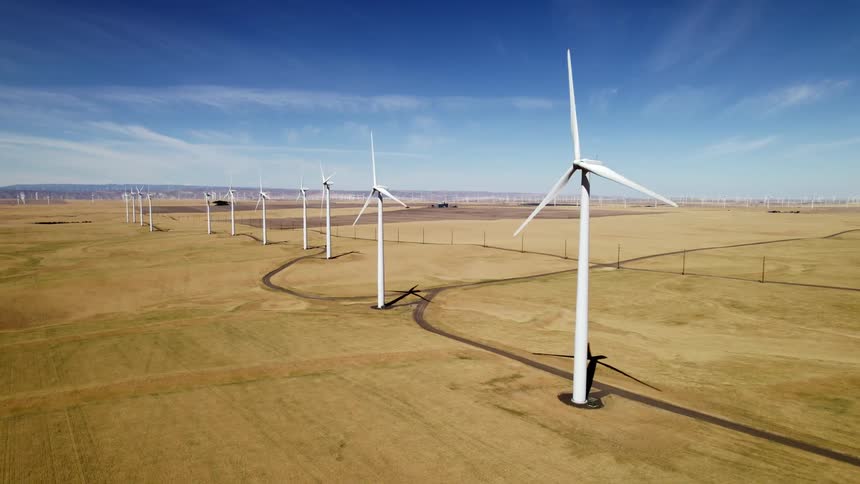 Aerial view of wind turbines slowly spinning on a wind farm in the fields under a blue sky