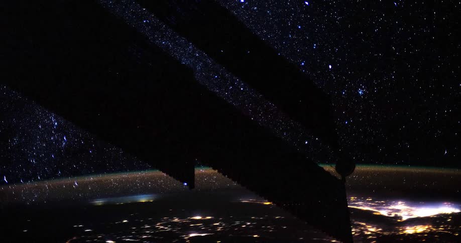 A satellite flies in space as lights flash on the earths surface as it glows among the stars