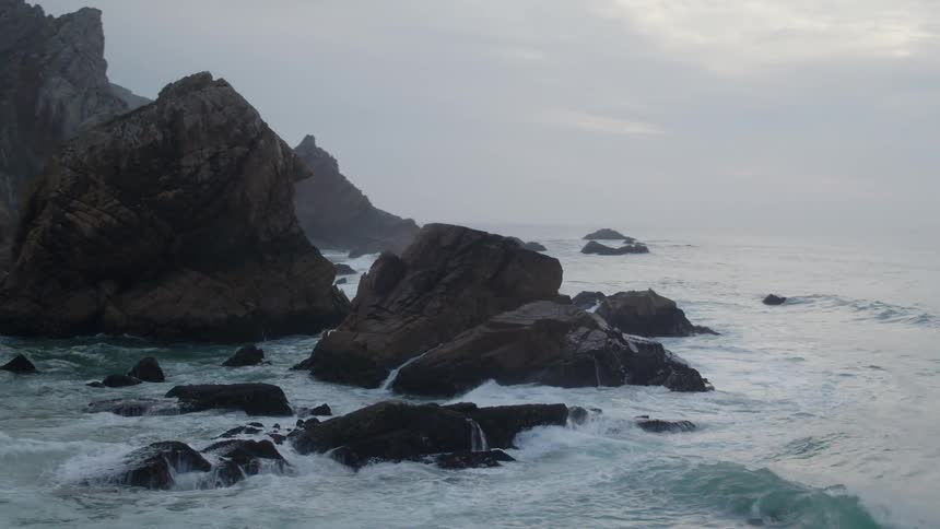 Waves crash against the rocks and sand of a shoreline