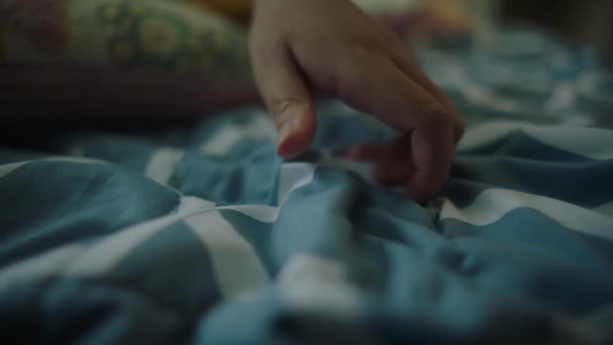 Close up of womans hand touching and holding light blue bed sheet in bedroom