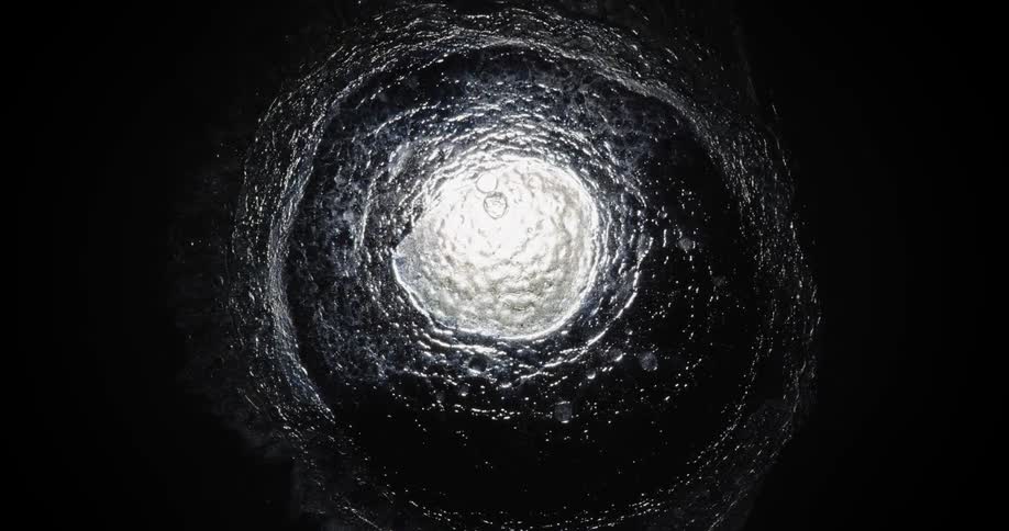 A single source of light is seen in the darkness beneath some churning water