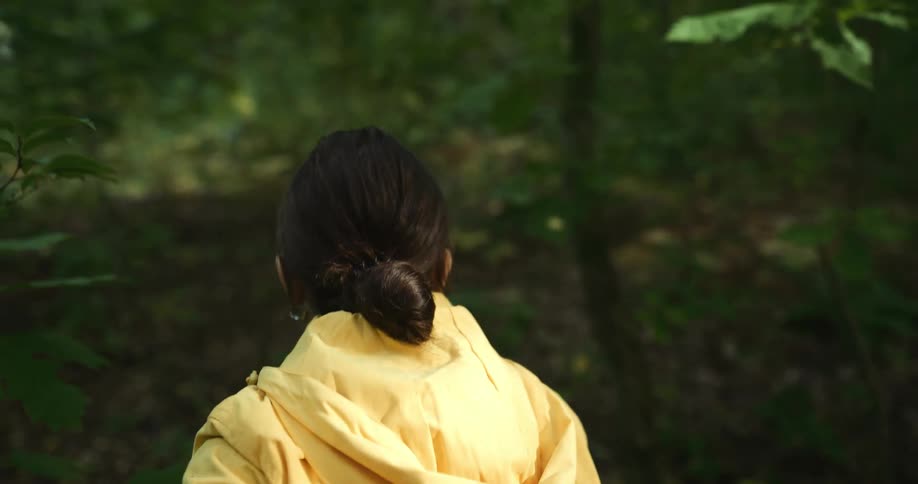Woman wearing earrings and yellow raincoat hikes in the green woods