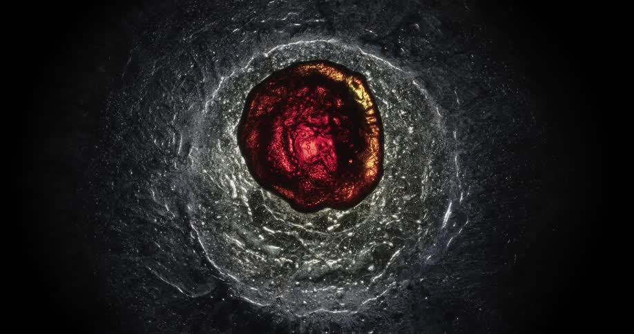 Crimson mixture tinted metallic forms rough circle in center of pale metallic substance that is in turn surrounded by dark mixture